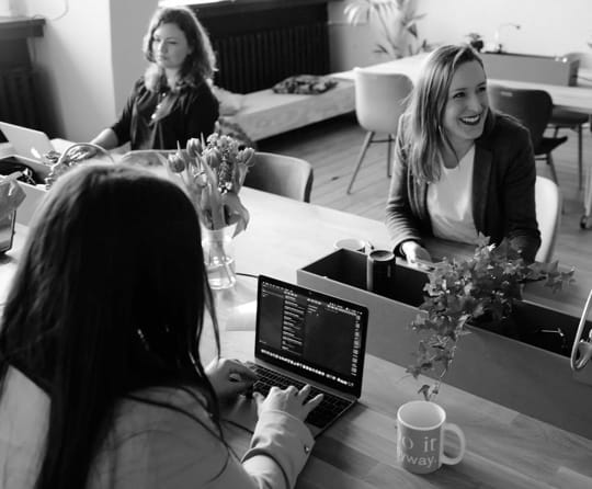 Three women working together at a desk with laptops and data analytics - Desktop view